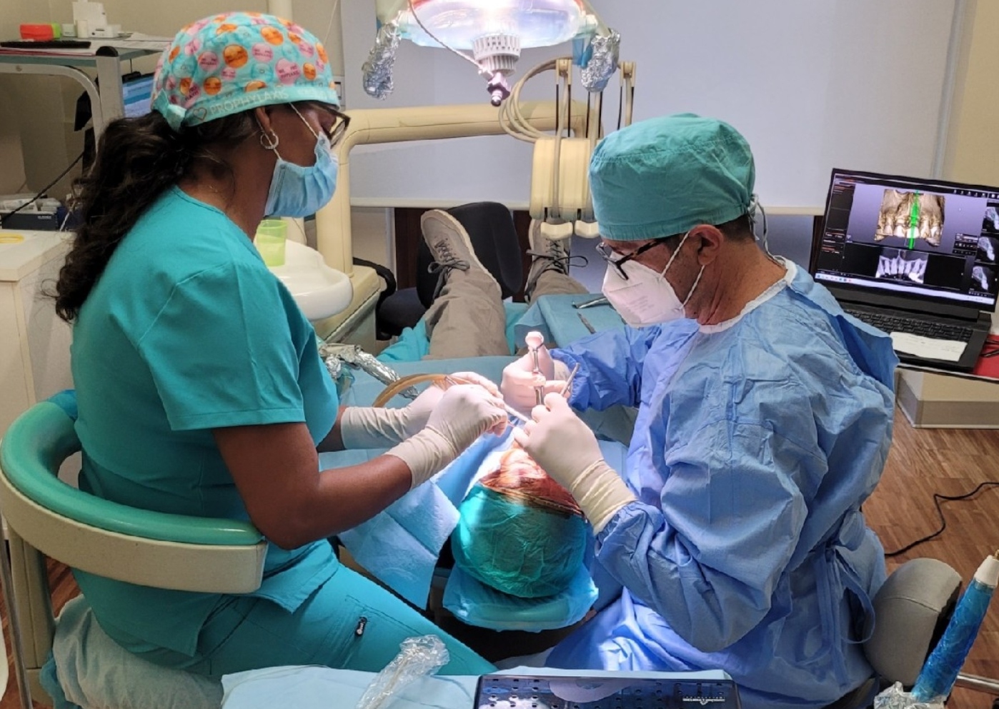 two surgeons in scrubs perform dental surgery on a patient under an overhead light using instruments
